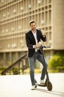 Young business man in a casual clothes receiving great news on mobile phone while standing on electric scooter by an office building photo