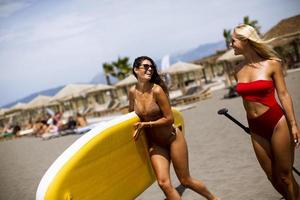 Two young women with paddle board on the beach on a summer day photo