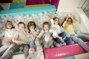 niños pequeños felices en la piscina de bolas sonriendo alegremente a la cámara mientras se divierten foto