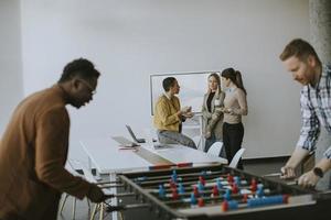 Young casual multiethnic business people playing table football and relaxing at office photo