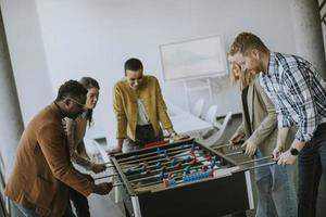 Young casual multiethnic business people playing table football and relaxing at office photo