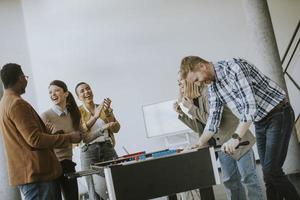 Young casual multiethnic business people playing table football and relaxing at office photo