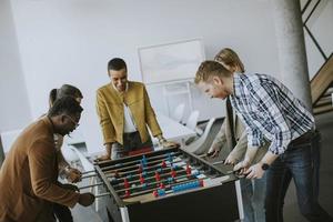 jóvenes empresarios multiétnicos casuales jugando futbolín y relajándose en la oficina foto