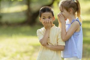 Caucasian girl telling secret to asian boy in the park photo