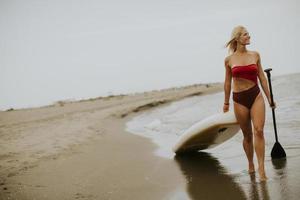 mujer joven caminando con paddle board en la playa en un día de verano foto