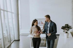 pareja de jóvenes empresarios caminando juntos y usando una tableta digital en la oficina moderna foto