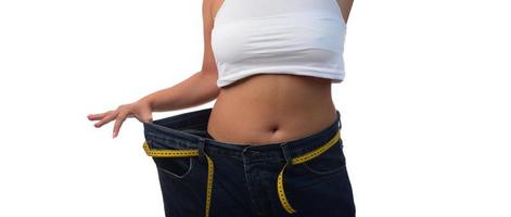 mid section of a woman with belly fat holding her blue jeans. Girl with big jeans isolated on white background. Woman shows her weight loss. Healthy lifestyle concept photo