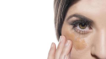 Portrait of a young woman applying liquid make up on her face. Isolated on white background photo