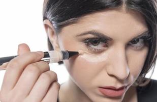 Portrait of a young woman applying liquid make up on her face. Isolated on white background photo