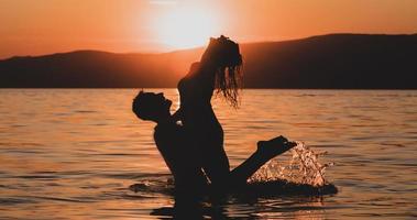 silhouettes in love romantic couple lovers hugging, kissing, touching, eye contact at sunset, sunrise on the background of the sea, the sun, the clouds in fiery red, orange colors photo