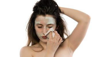 Beautiful young woman with towel wrapped around her head applying clay face mask at the bathroom photo