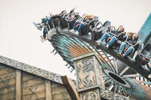 people having fun in amusement park. Young friends on thrilling roller coaster ride photo