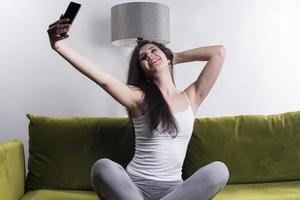 mujer feliz escuchando música desde el teléfono móvil mientras se sienta en la alfombra al lado del sofá en las casas, niña sonriente relajándose con auriculares por la mañana, hora de relajarse. foto