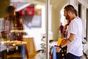 Portrait of cheerful Caucasian young couple man and woman holding many paper bags after shopping while walking and talking on street. Happy family couple with packages outdoor. Buying concept photo