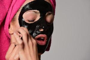 hermosa modelo femenina con máscara cosmética facial negra. aislado sobre fondo gris foto