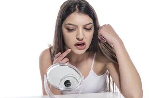 Portrait of a girl putting cosmetic ointment on face while watching at mirror indoor photo