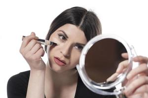 Portrait of a young woman applying liquid make up on her face. Isolated on white background photo