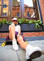 hermosa chica hipster con patineta con gafas de sol en la ciudad. foto