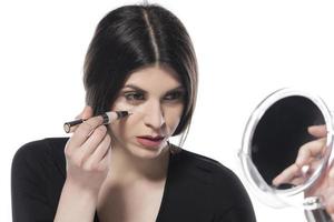 Portrait of a young woman applying liquid make up on her face. Isolated on white background photo