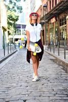 Beautiful hipster girl with skate board wearing sunglasses in the city. photo