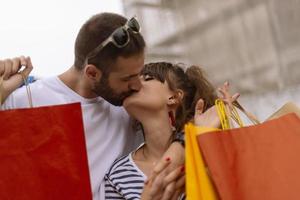 retrato de una alegre pareja joven caucásica hombre y mujer sosteniendo muchas bolsas de papel después de ir de compras mientras camina y habla en la calle. feliz pareja familiar con paquetes al aire libre. concepto de compra foto