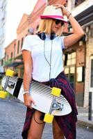 hermosa chica hipster con patineta con gafas de sol en la ciudad. foto