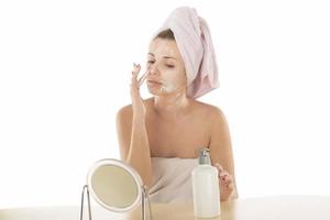 Attractive young adult woman apply facial cream look in mirror, beautiful healthy lady wrapped in towels put moisturizing lifting nourishing day creeme on soft hydrated moisturized skin in bathroom photo