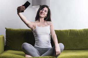 mujer feliz escuchando música desde el teléfono móvil mientras se sienta en la alfombra al lado del sofá en las casas, niña sonriente relajándose con auriculares por la mañana, hora de relajarse. foto