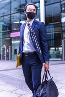 Handsome Asian businessman wearing covid mask and suit, walking outdoors, successful manager during break walking in the city. photo