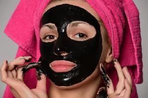 beautiful female model with black facial cosmetic mask. Isolated on gray background photo