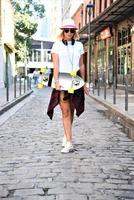 Beautiful hipster girl with skate board wearing sunglasses in the city. photo