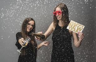 Two female friends celebrating New Year with confetti and champagne holding sign. isolated photo