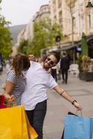 retrato de una alegre pareja joven caucásica hombre y mujer sosteniendo muchas bolsas de papel después de ir de compras mientras camina y habla en la calle. feliz pareja familiar con paquetes al aire libre. concepto de compra foto