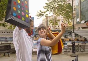 Portrait of cheerful Caucasian young couple man and woman holding many paper bags after shopping while walking and talking on street. Happy family couple with packages outdoor. Buying concept photo