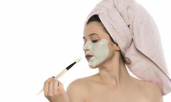 Beautiful woman having clay facial mask apply by beautician. photo