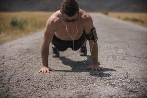 atleta masculino ejerciendo push up afuera bajo el sol soleado. ajuste el modelo de fitness masculino sin camisa en el ejercicio de crossfit al aire libre. concepto de estilo de vida saludable. foto