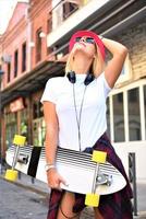 hermosa chica hipster con patineta con gafas de sol en la ciudad. foto