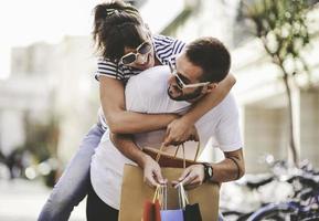 Portrait of cheerful Caucasian young couple man and woman holding many paper bags after shopping while walking and talking on street. Happy family couple with packages outdoor. Buying concept photo