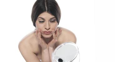 beautiful attractive brunette woman checking her face skin in front of a mirror on white background. photo