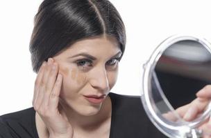Portrait of a young woman applying liquid make up on her face. Isolated on white background photo