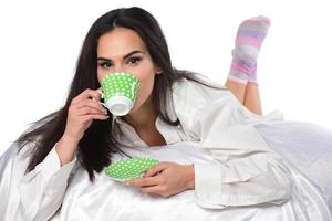 Cheerful tender female sitting with cup of coffee on be photo