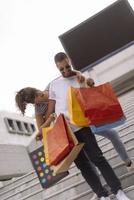 Portrait of cheerful Caucasian young couple man and woman holding many paper bags after shopping while walking and talking on street. Happy family couple with packages outdoor. Buying concept photo