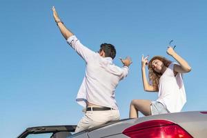 Friends having fun at car trip around the world. Couple in love with arms up on a convertible car. photo