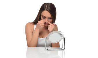 Acne prone skin concept. Young woman looking at mirror at home, checking her face skin photo