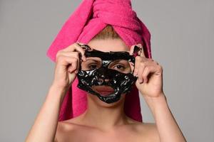 beautiful female model with black facial cosmetic mask. Isolated on gray background photo