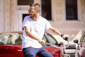 Handsome man is using a smart phone and smiling while riding bicycle in city photo