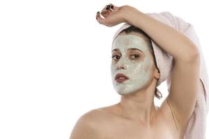 Beautiful young woman with towel wrapped around her head applying clay face mask at the bathroom photo