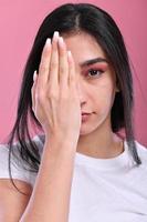 foto de una mujer joven y atractiva que cubre el brazo del ojo chequeo oftalmología de la visión aislada sobre fondo de color rosa