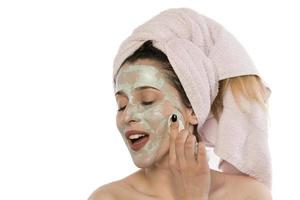 Beautiful young woman with towel wrapped around her head applying clay face mask at the bathroom photo