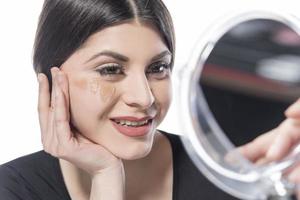 Portrait of a young woman applying liquid make up on her face. Isolated on white background photo